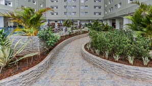 A courtyard with a stone pathway, surrounded by various plants and a multi-story building in the background. - Capital O 93516 Loftvilles City Residence (Tangerang)