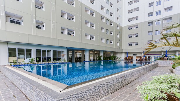 A modern hotel with a central swimming pool, multiple balconies, and a well-maintained garden area. - Capital O 93516 Loftvilles City Residence (Tangerang)