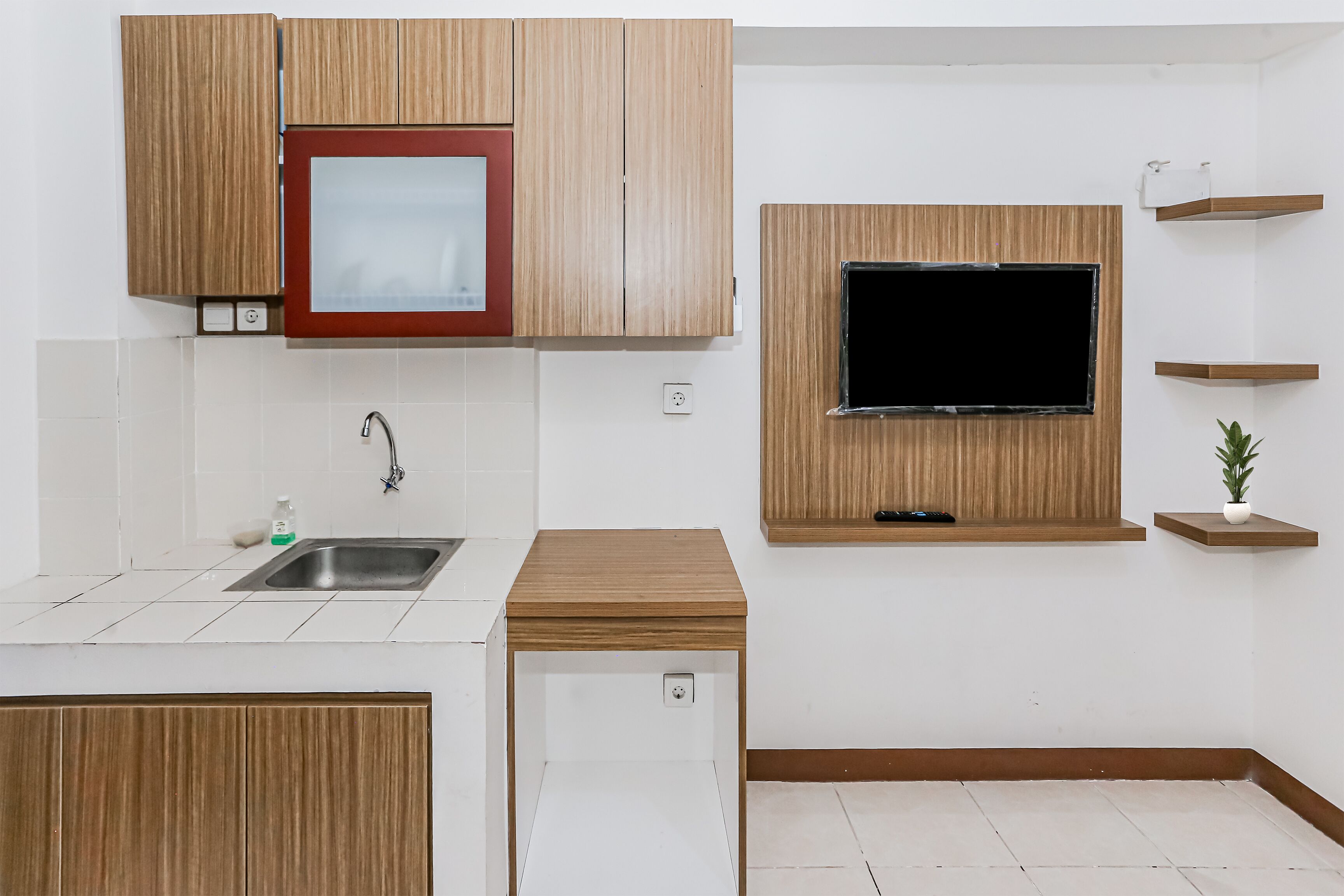 A compact kitchen with wooden cabinets, a built-in TV, a small sink, and a potted plant.