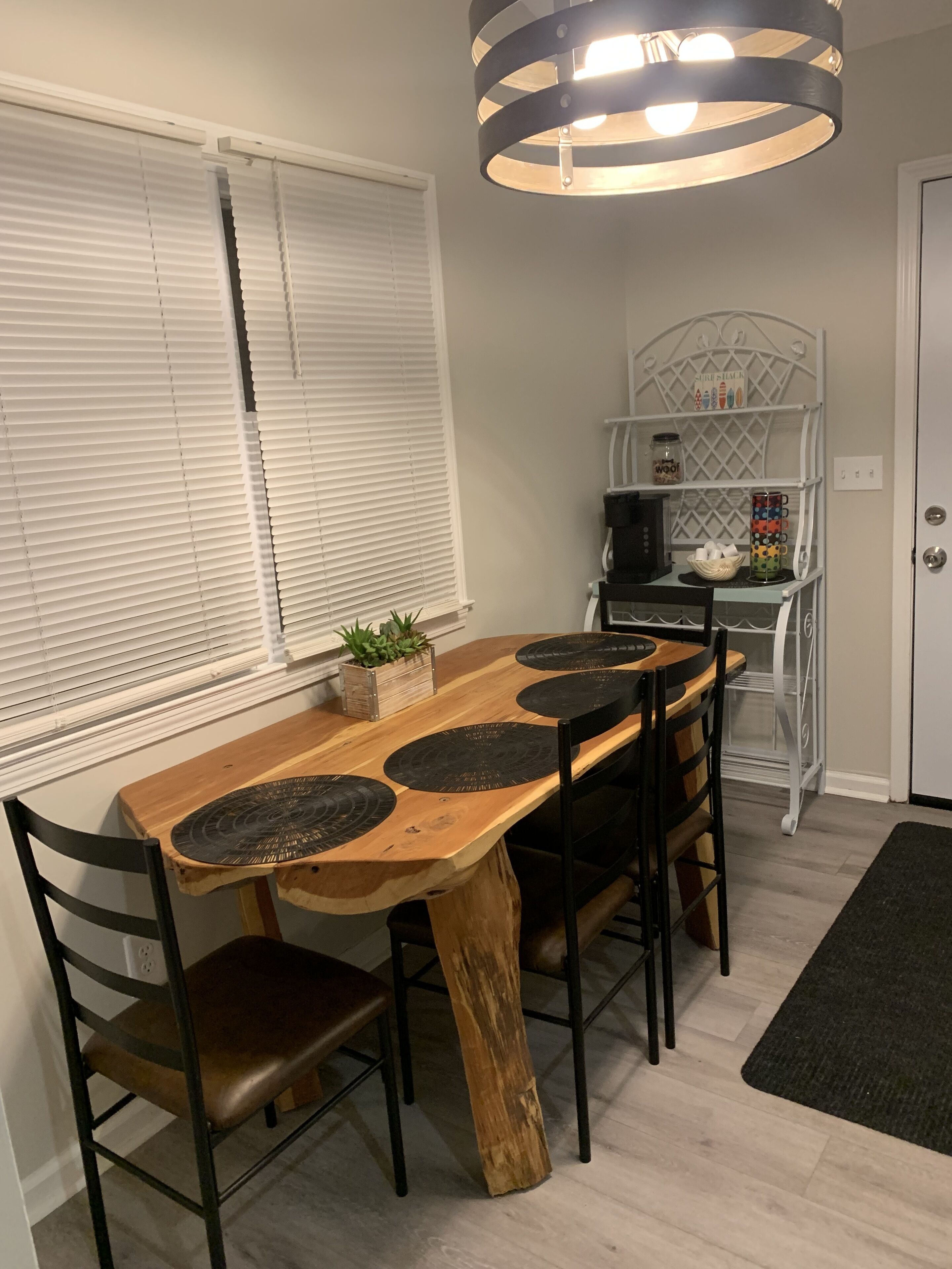En matplats med ett träbord, svarta stolar och en hängande lampa.