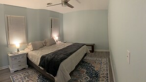 Ein Schlafzimmer mit einem Bett, Nachttischen, einer Lampe, einem Deckenventilator und einem gemusterten Teppich.