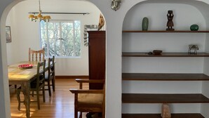 A dining area with a wooden table and chairs, a chandelier, and a window with a view of trees.