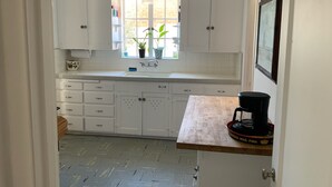 A kitchen with white cabinets, a window with plants, a sink, and a coffee maker on a wooden counter.