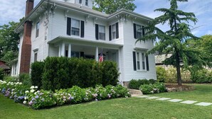 A two-story white house with a brick chimney, a front porch, and a flag. - Spacious Guest House in Falmouth Village (Falmouth)