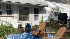 A patio with two wooden Adirondack chairs, a blue patterned rug, and potted plants. - Spacious Guest House in Falmouth Village (Falmouth)