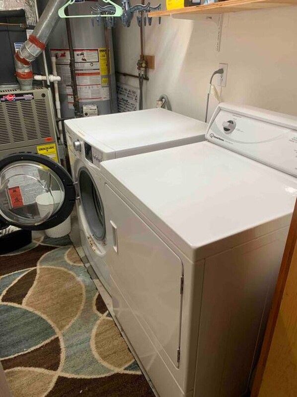 A laundry room with a front-loading washer and dryer, a utility room with a water heater, and a patterned rug on the floor. - Spacious Guest House in Falmouth Village (Falmouth)