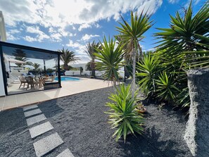 A modern outdoor patio with a pool, surrounded by tropical plants and a glass enclosure. - Casa Del Faro, private heated pool & air conditioning close to amenities (Playa Blanca)