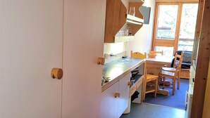 Une cuisine compacte avec des meubles en bois, un coin repas avec une table et des chaises, et une vue par la fenêtre.
