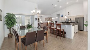 Eine moderne Küche mit weißen Schränken, einem Edelstahlkühlschrank und einem Essbereich mit Glastisch und Stühlen.