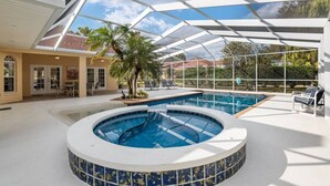 Ein überdachter Pool mit Whirlpool, Liegestühlen und Palmen.
