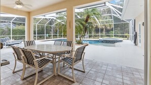 Eine überdachte Terrasse mit einem runden Tisch und Stühlen, einem Pool und Blick auf Palmen.
