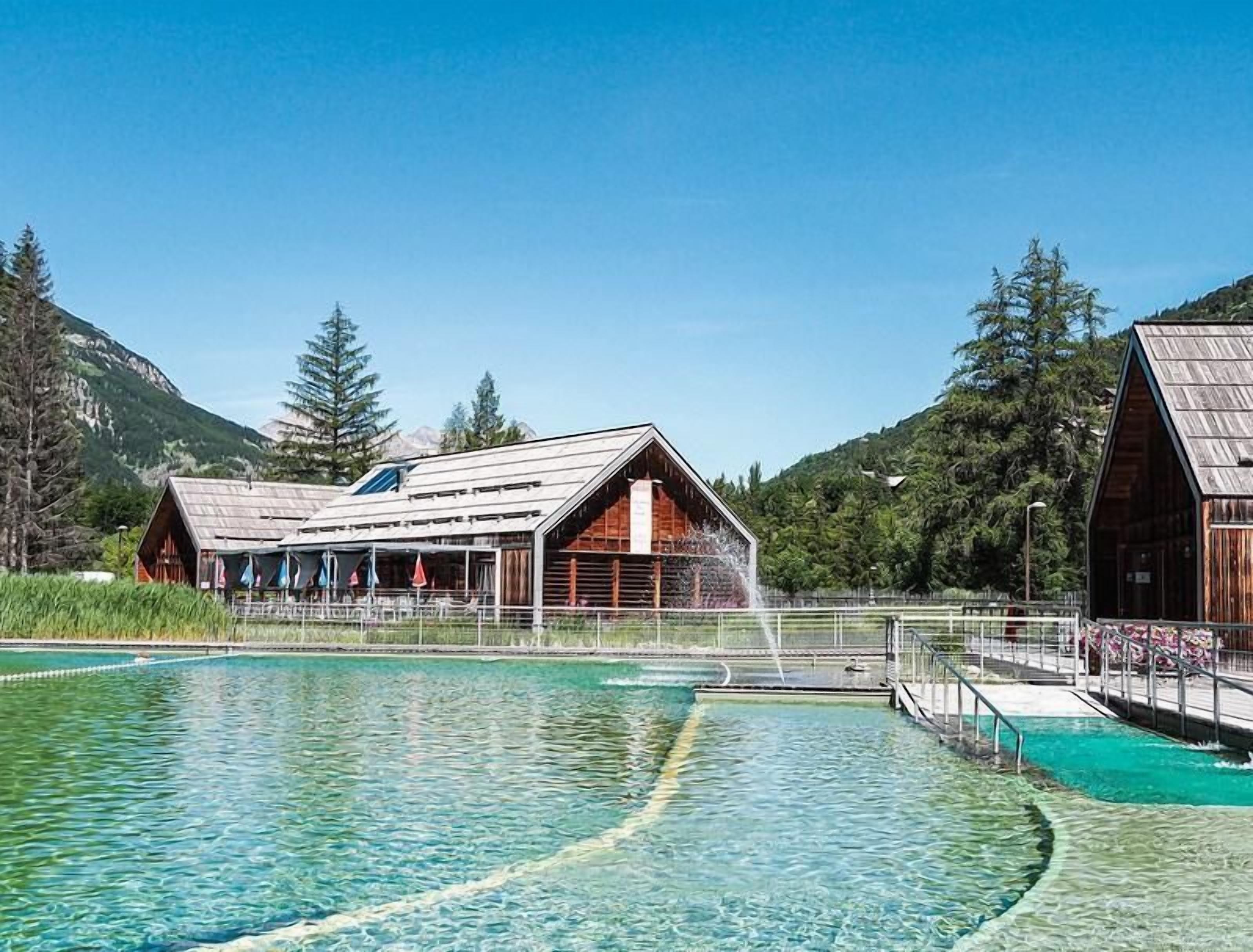 A pool area with wooden buildings, a bridge, and a mountainous backdrop.