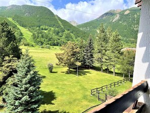 Un paisaje montañoso con un campo cubierto de hierba, árboles y un edificio de fachada blanca.