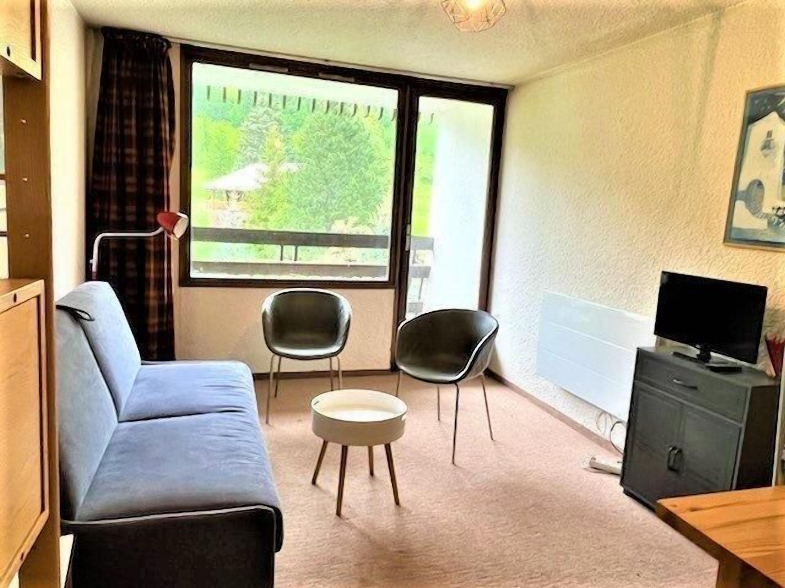 A small, furnished room with a sofa, two chairs, a television, and a cabinet.