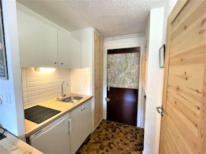 A compact kitchen with white cabinets, a black countertop, and a wooden door. - 100m from resort center, 2nd floor, swimming pool, tv, 17m², Serre Chevalier (SERRE CHEVALIER)