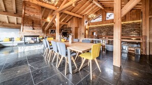 A spacious wooden interior with a dining area, stone fireplace, and a kitchen visible in the background. - Heavenly - Luxurious chalet with jacuzzi and sauna (Montriond)