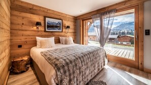 A bedroom with a large bed, wooden walls, a window with a view of mountains, and two wall-mounted lamps. - Heavenly - Luxurious chalet with jacuzzi and sauna (Montriond)