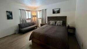 A bedroom with a large bed, a sofa, and a nightstand. - Wagner Creek Hideaway (Munising Township)