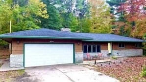 A single-story house with a garage, surrounded by trees and a yard. - Wagner Creek Hideaway (Munising Township)