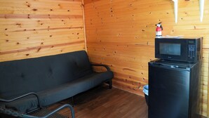 A wooden cabin interior with a sofa, a small black refrigerator, and a microwave on top of it. - Franky and Louie's Turquoise Cabin 3 (Sunrise Beach)