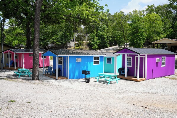 Une rangée de maisons mobiles aux couleurs vives, avec des tables de pique-nique et un sol recouvert de gravier.