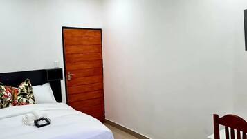 Una camera d'albergo con un letto, una porta in legno, una TV fissata al muro e una sedia con fiori.