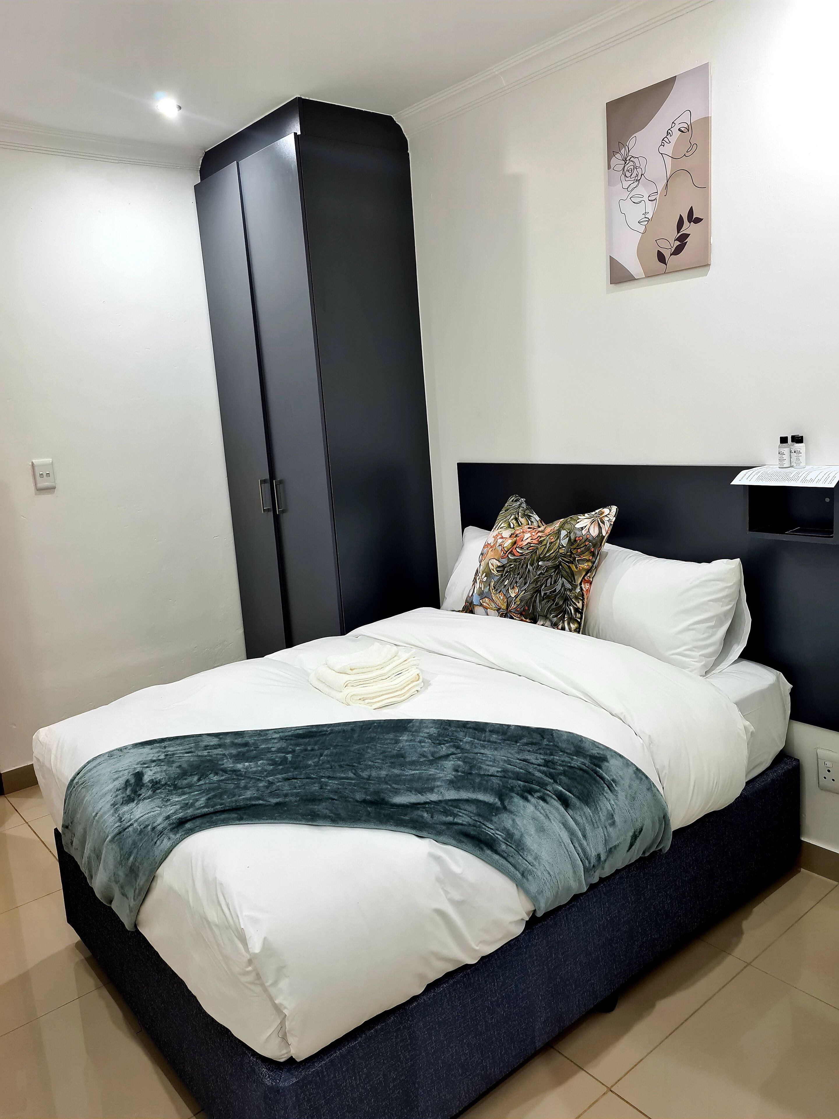 Een moderne slaapkamer met een groot bed, een garderobe, een hoofdeinde met plank en een kunstwerk aan de muur.