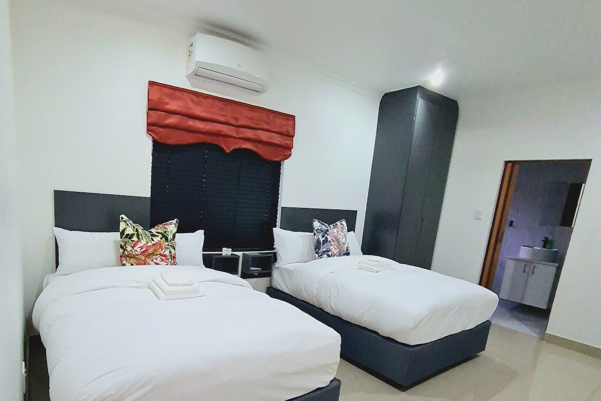 Une chambre d’hôtel avec deux lits, un couvre-lit rouge au-dessus de la tête de lit et un appareil de climatisation blanc fixé au mur.