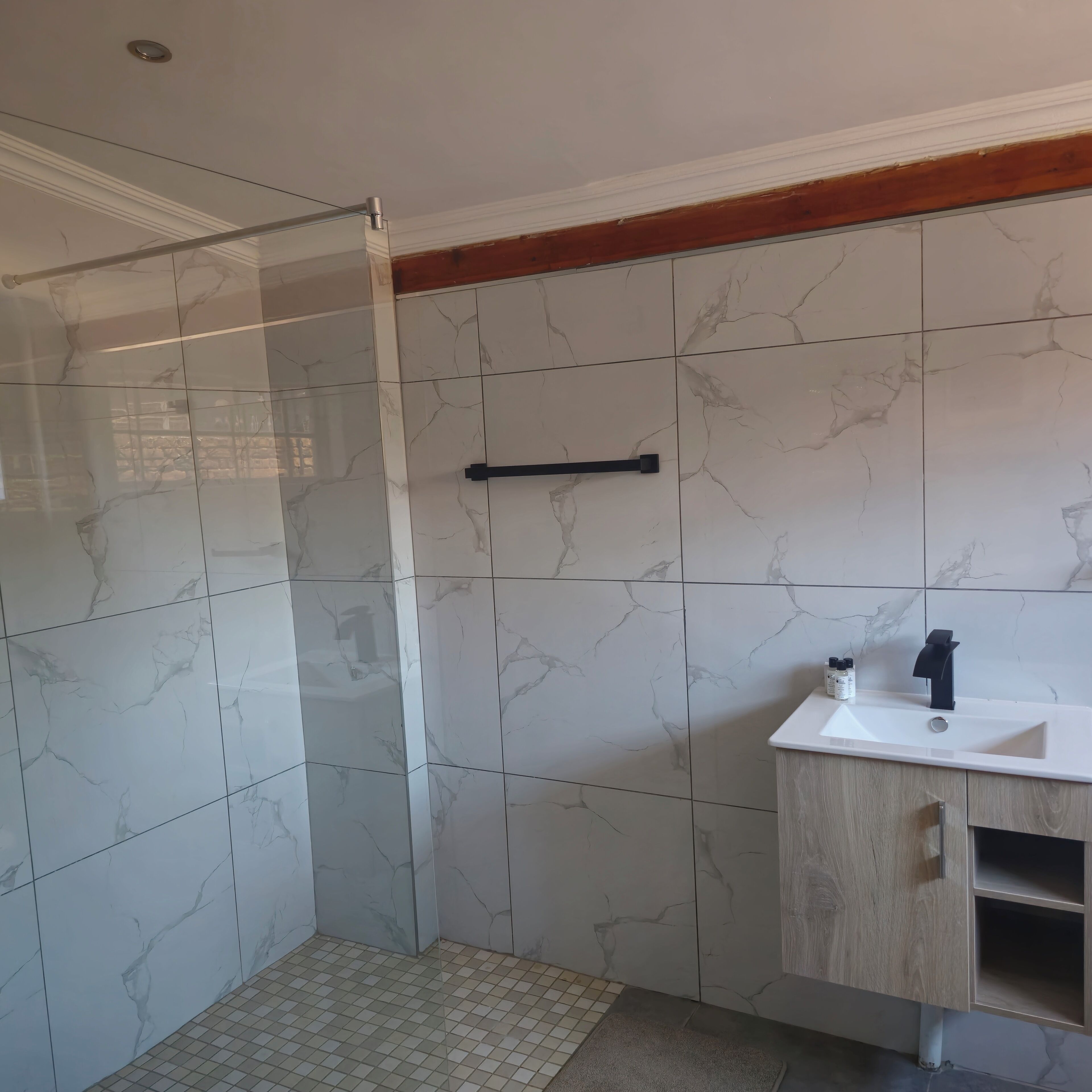 Un baño con baldosas de mármol blanco, cabina de ducha de vidrio, tocador de madera con lavamanos y un perchero.