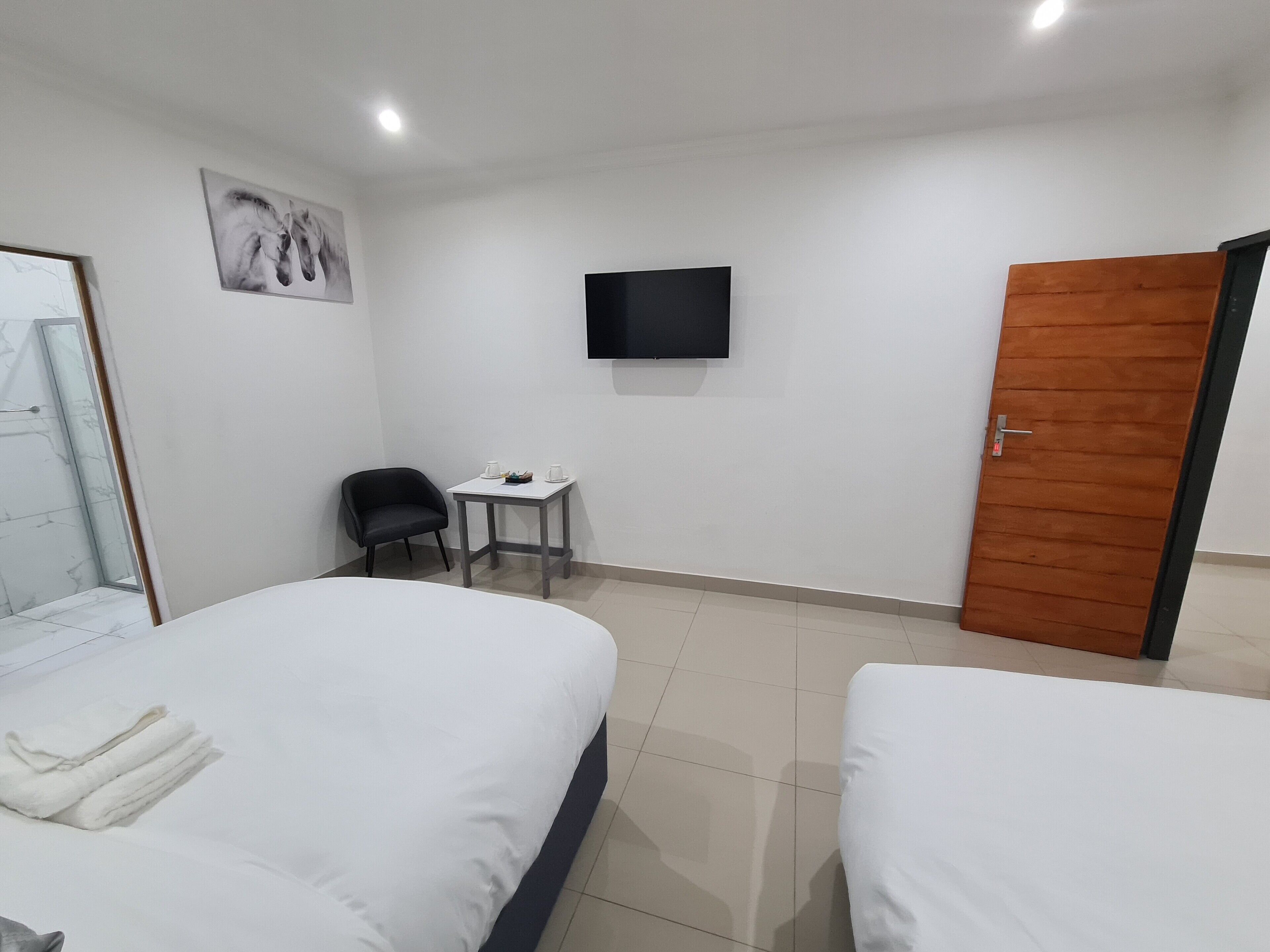 A hotel room with two beds, a small table with a chair, a TV mounted on the wall, and a wooden door.