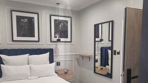 Een moderne slaapkamer met een groot bed, een nachtkastje, een spiegel en lijstwerken aan de muur.