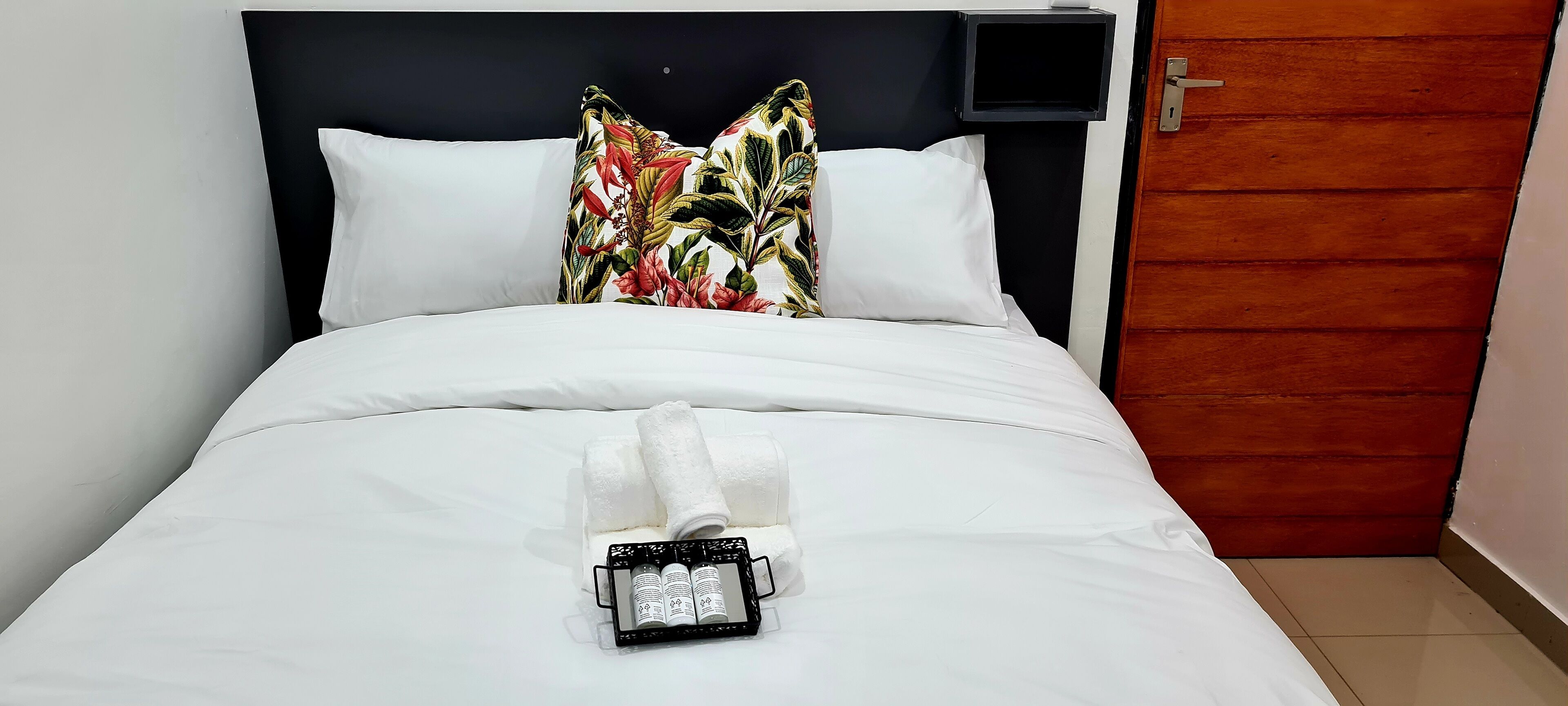 A neatly made bed with white linens, a floral pillow, and a tray with toiletries.