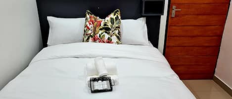 A neatly made bed with white linens, a floral pillow, and a tray with toiletries.