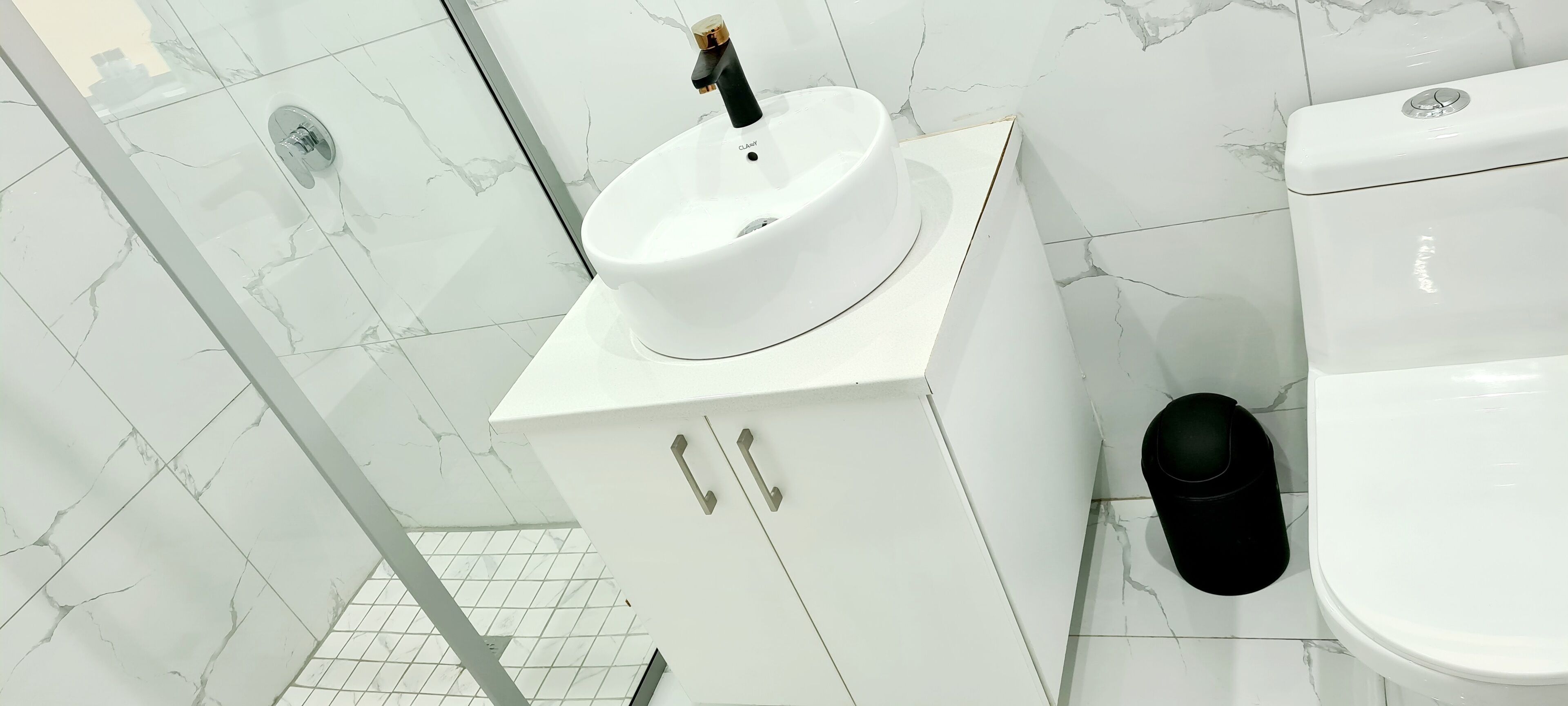 A bathroom with a white sink, toilet, and a black trash bin.