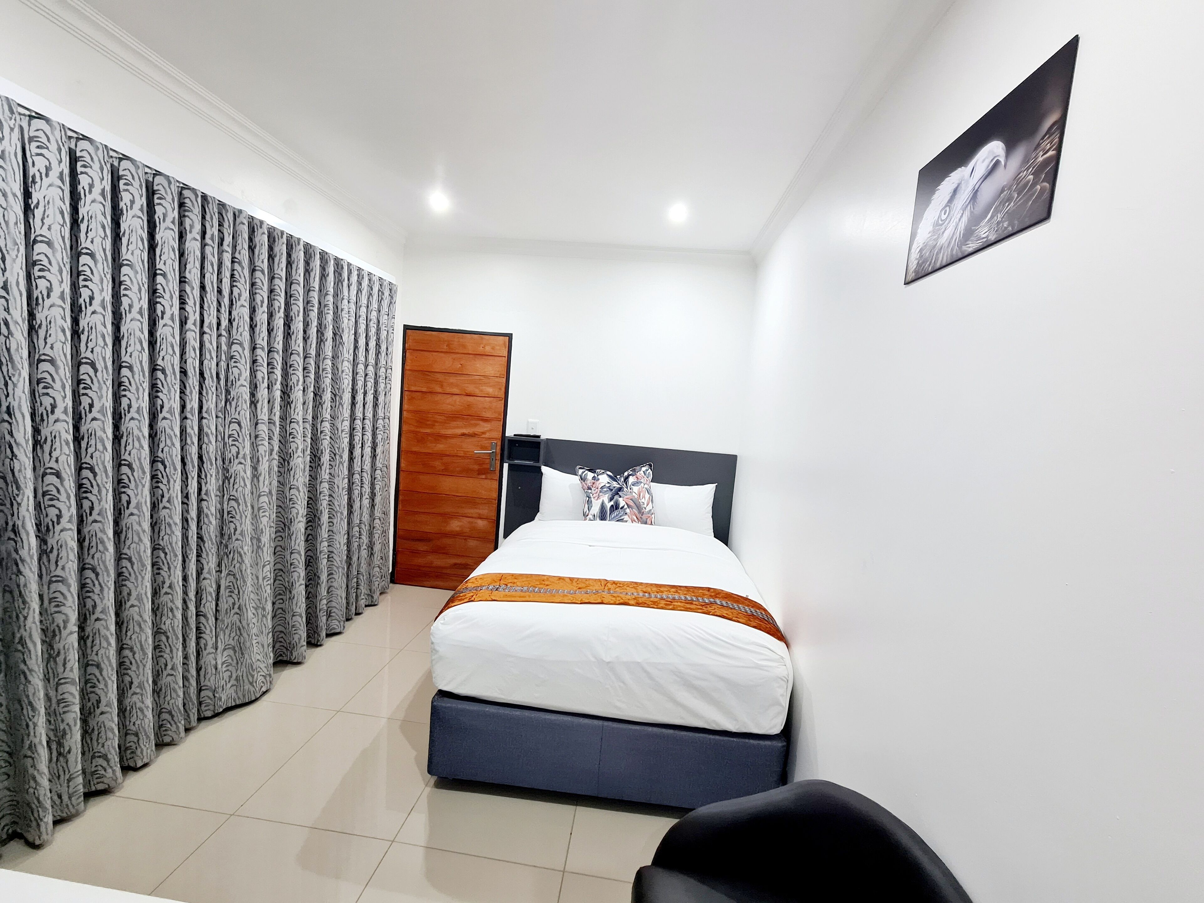 Une chambre d’hôtel avec un lit, des rideaux, une porte en bois et un tableau accroché au mur.