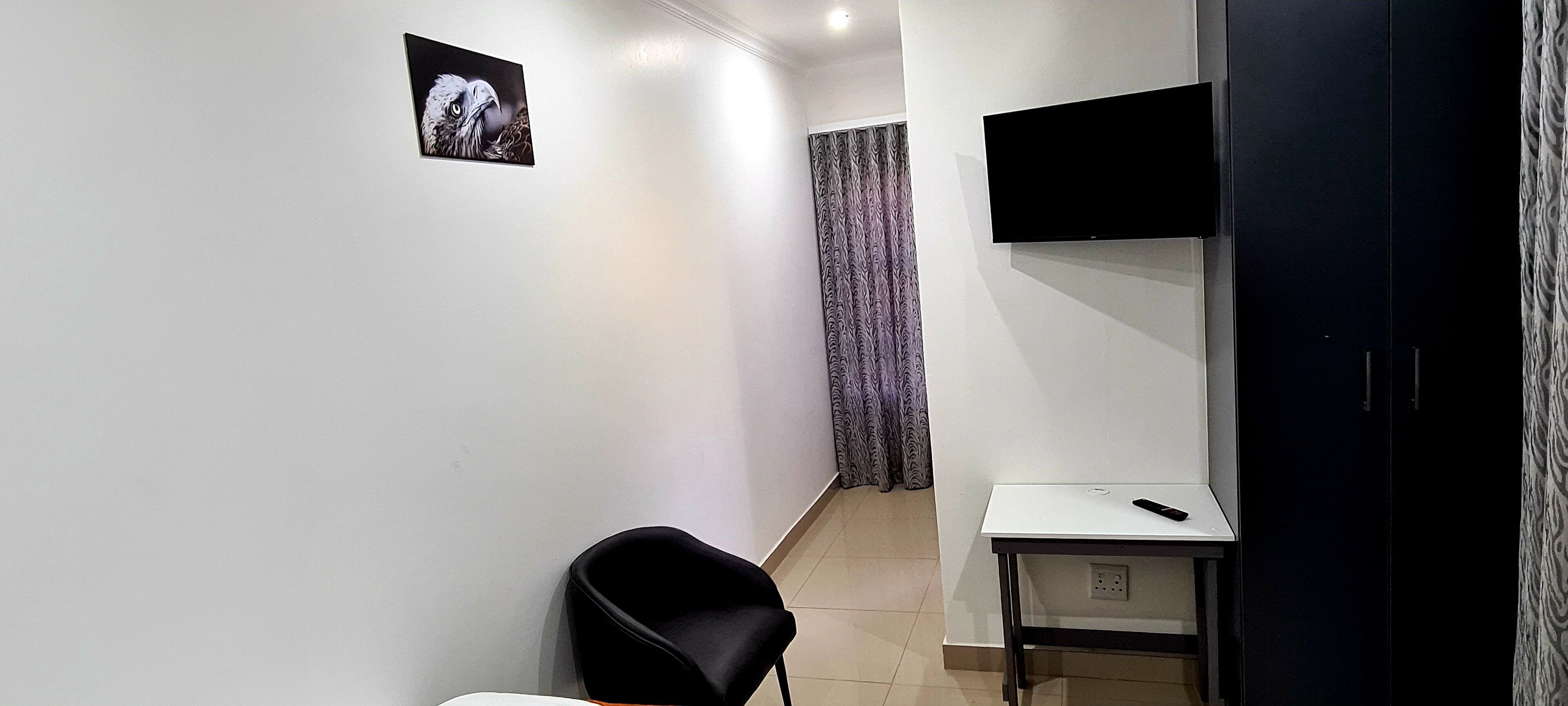 A hotel room with a bed, a desk, a chair, a TV mounted on the wall, and a curtain.