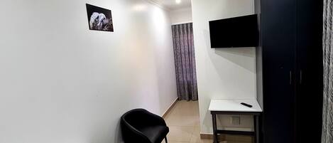 A hotel room with a bed, a desk, a chair, a TV mounted on the wall, and a curtain.