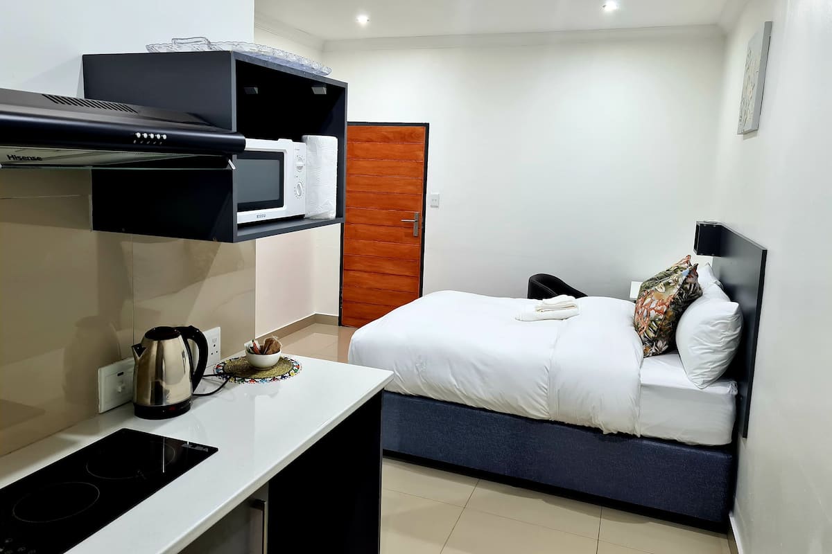 Une chambre d’hôtel moderne équipée d’un lit, d’un bureau avec une bouilloire, d’un four à micro-ondes et d’une petite table avec une tasse.