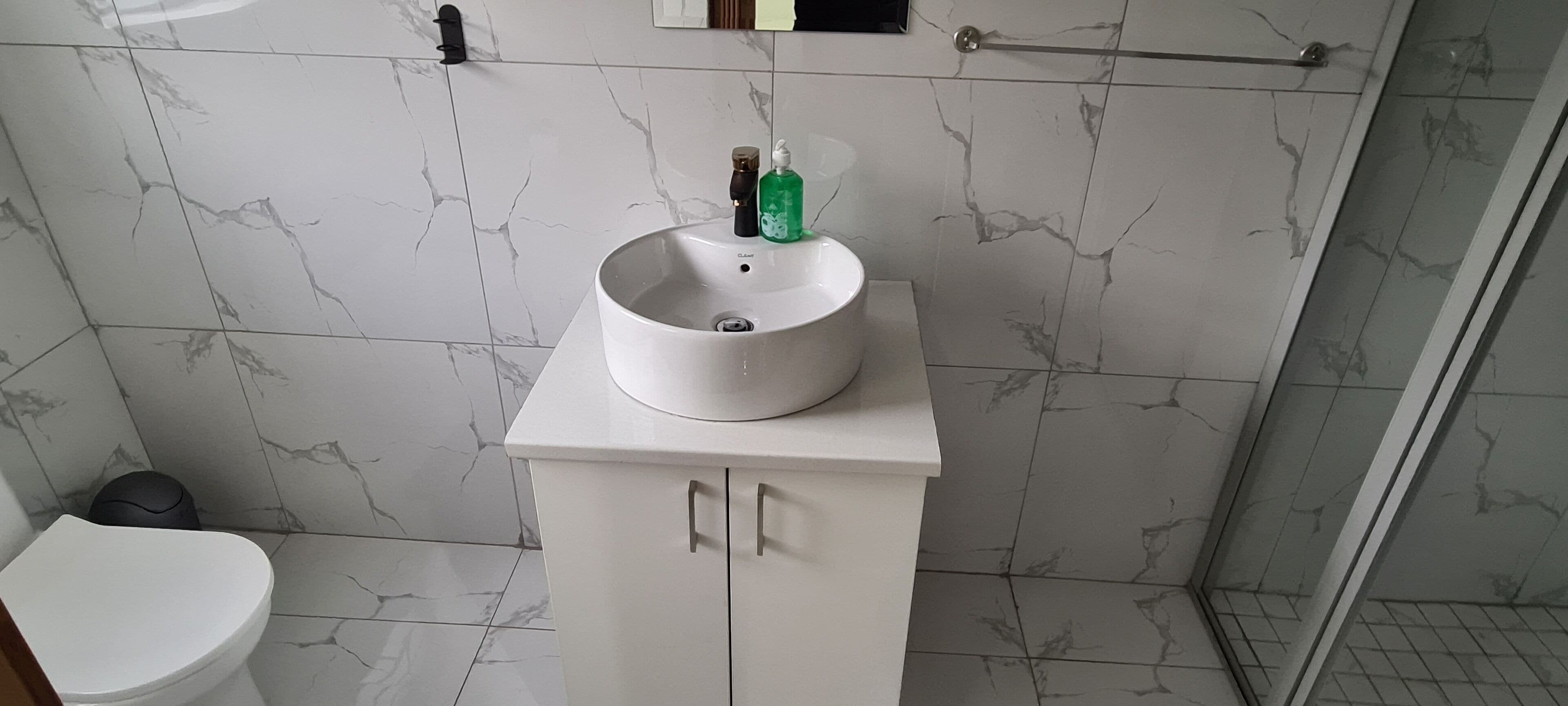 Une salle de bain avec un lavabo blanc sur un piédestal, des toilettes et un espace douche.