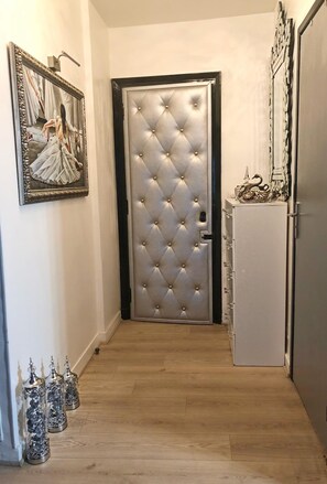 Stylish hallway leads to a door, flanked by artwork and a decorative cabinet.