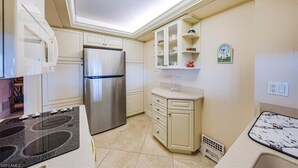 Una cocina compacta con muebles blancos, un refrigerador de acero inoxidable, un horno empotrado y una encimera de mármol.