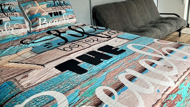 Een slaapkamer met een bed, een grijze fauteuil, een wanddecoratie en een koelkast.