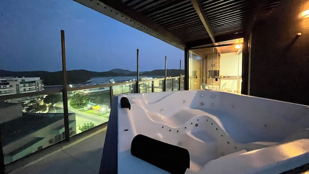 Un hidromasaje moderno al aire libre con vistas a un paisaje urbano y montañas al atardecer.