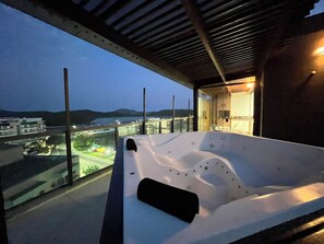 Un hidromasaje moderno al aire libre con vistas a un paisaje urbano y montañas al atardecer.