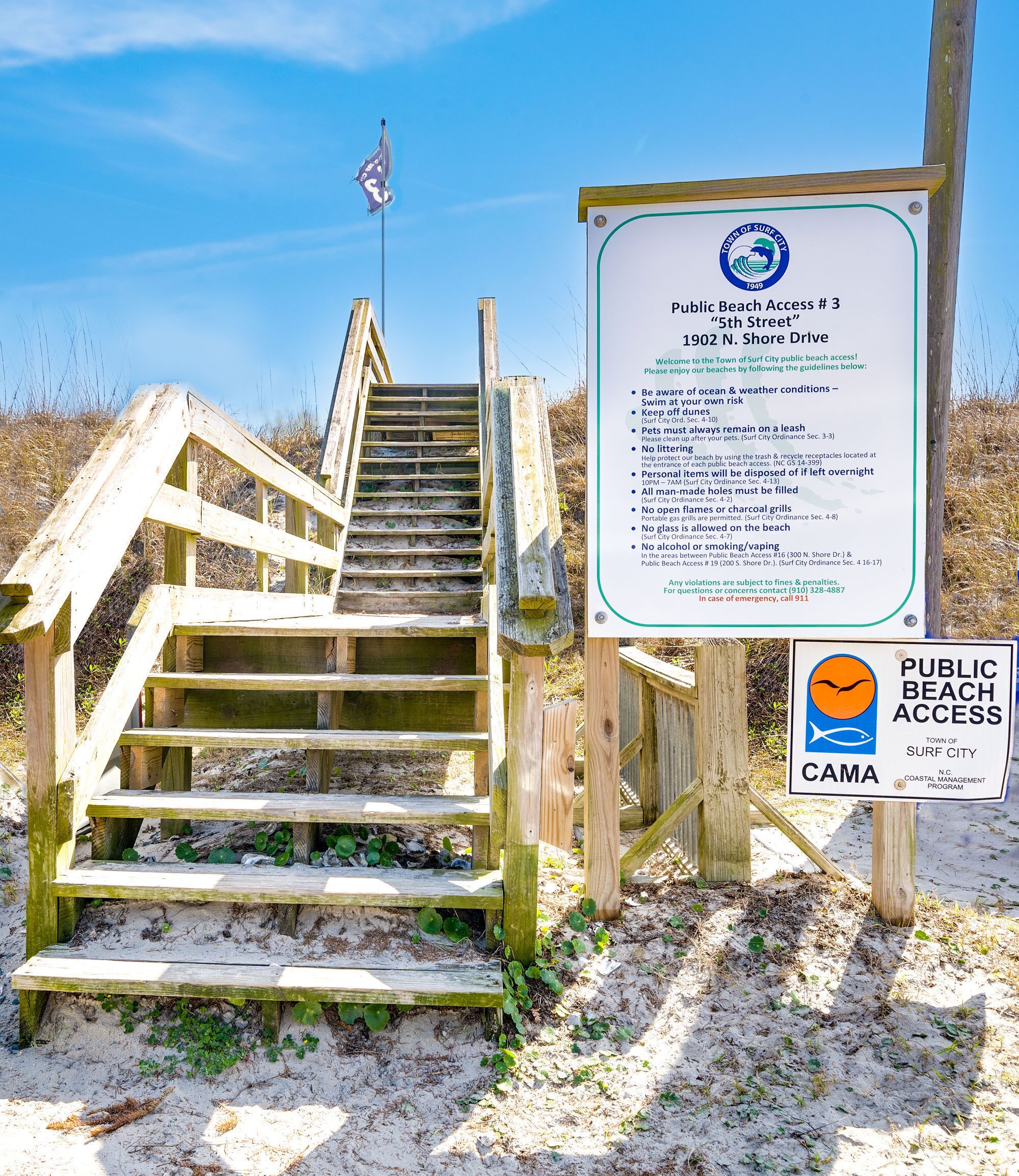 Un escalier en bois mène à une plage où un panneau indique les règles d’accès à la plage.