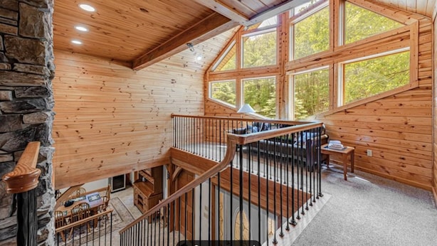 A wooden cabin interior with a stone wall, a staircase, and large windows offering a view of trees. - Perfect Mountain Retreat; minutes from all the Laurel Highlands has to offer! (Somerset)