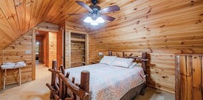 A wooden cabin bedroom with a bed, a ceiling fan, and a small table with towels.