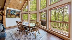 A dining area with a large table and chairs, surrounded by large windows offering a view of the forest. - Perfect Mountain Retreat; minutes from all the Laurel Highlands has to offer! (Somerset)