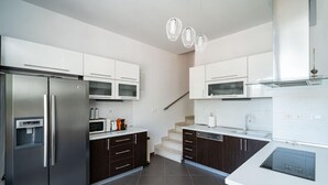 A modern kitchen with stainless steel appliances, dark wood cabinets, white countertops, and a staircase leading to another level. - Villa with Swim/Heated Pool and charming Bay view (Zaton)