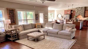 A spacious living room with a large sectional sofa, a small ottoman, and a kitchen area in the background. - Beautiful 5 BR, 3 BA, home only minutes away from the Masters and Peach Jam! (North Augusta)